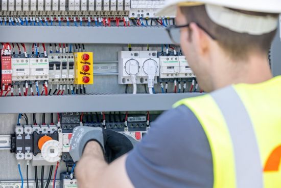 Junger Mitarbeiter steckt verschiedene Kabel um und trägt Sicherheitskleidung.