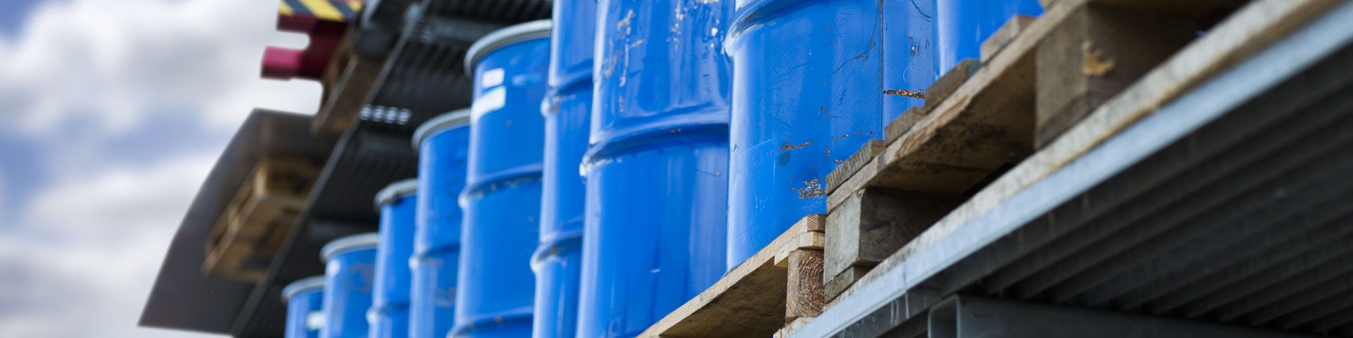 Mehrere blaue Metallfässer stehen gestapelt vor einer industriellen Verladeeinrichtung.