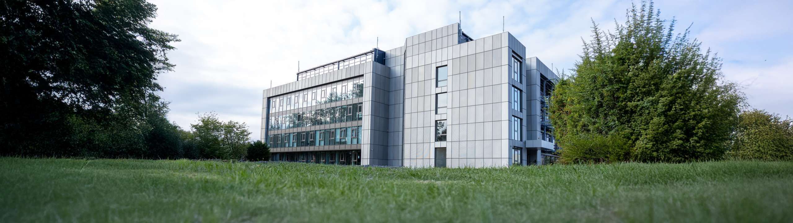 Ein großes und modernes Bürogebäude, dass von einer grünen Wiese umgeben ist.